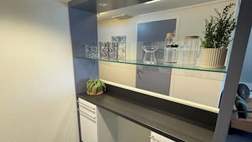 Una kitchenette compacta con un estante de vidrio, gabinetes blancos y una planta en maceta.