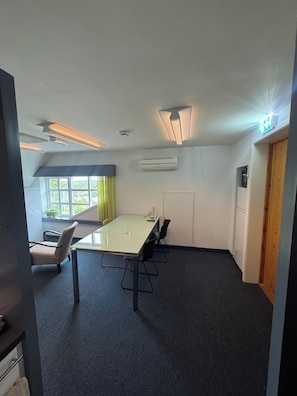 A conference room with a table, chairs, a window with curtains, an air conditioning unit, and a door.
