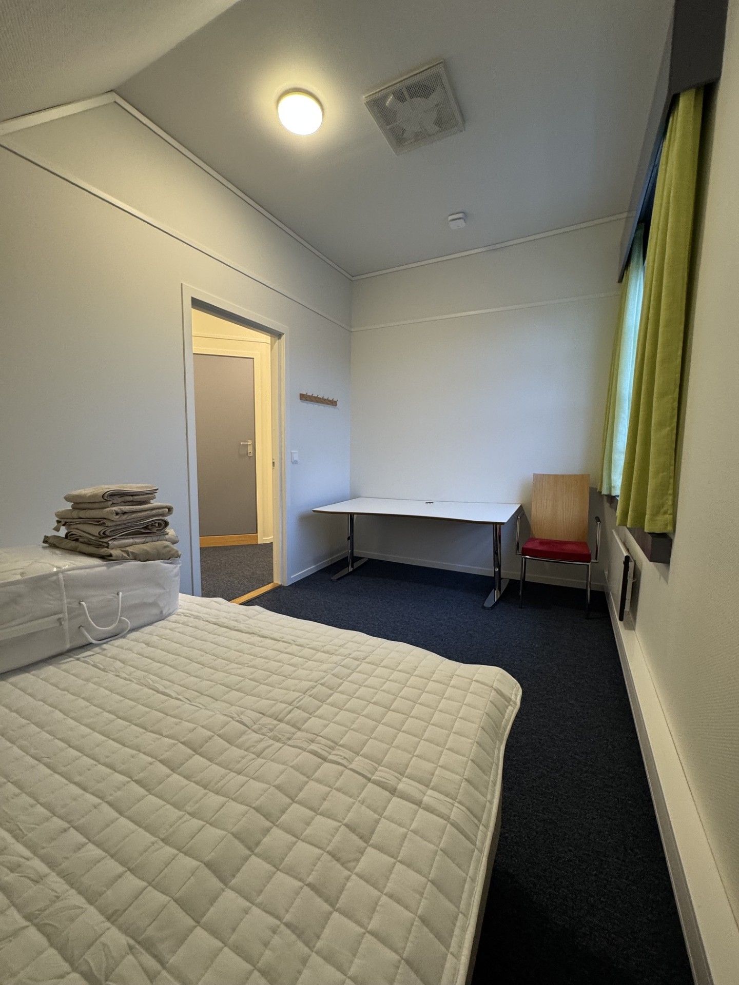 Habitació d'hotel amb llit, escriptori, cadira i finestra amb cortines.