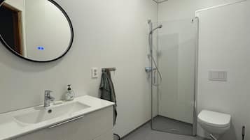 Un baño moderno con lavamanos, espejo y inodoro blancos.