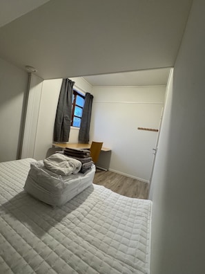 A bedroom with a bed, a window with curtains, a chair, and a coat rack.