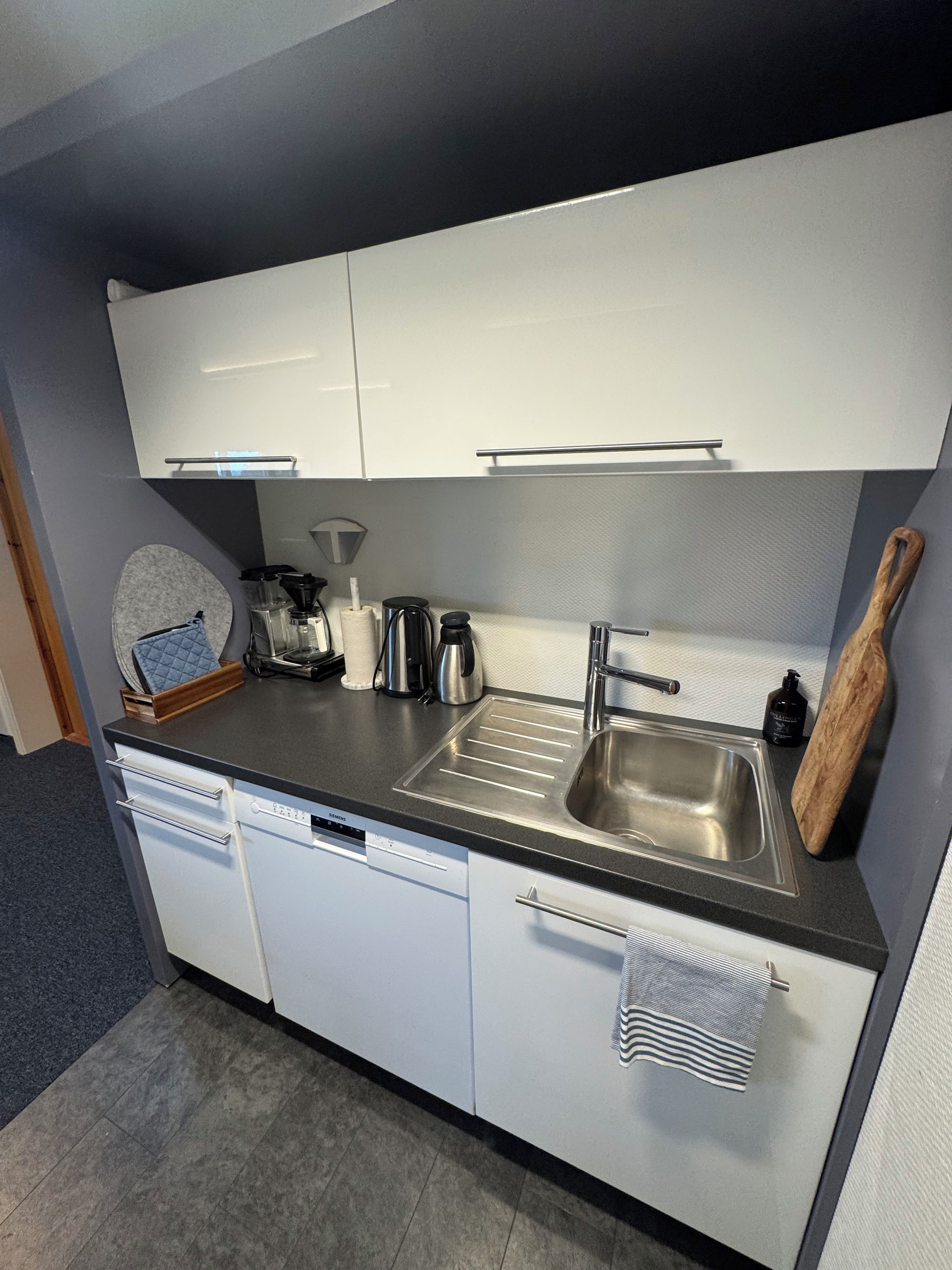 A compact kitchen with white cabinets, a stainless steel sink, and a dishwasher.