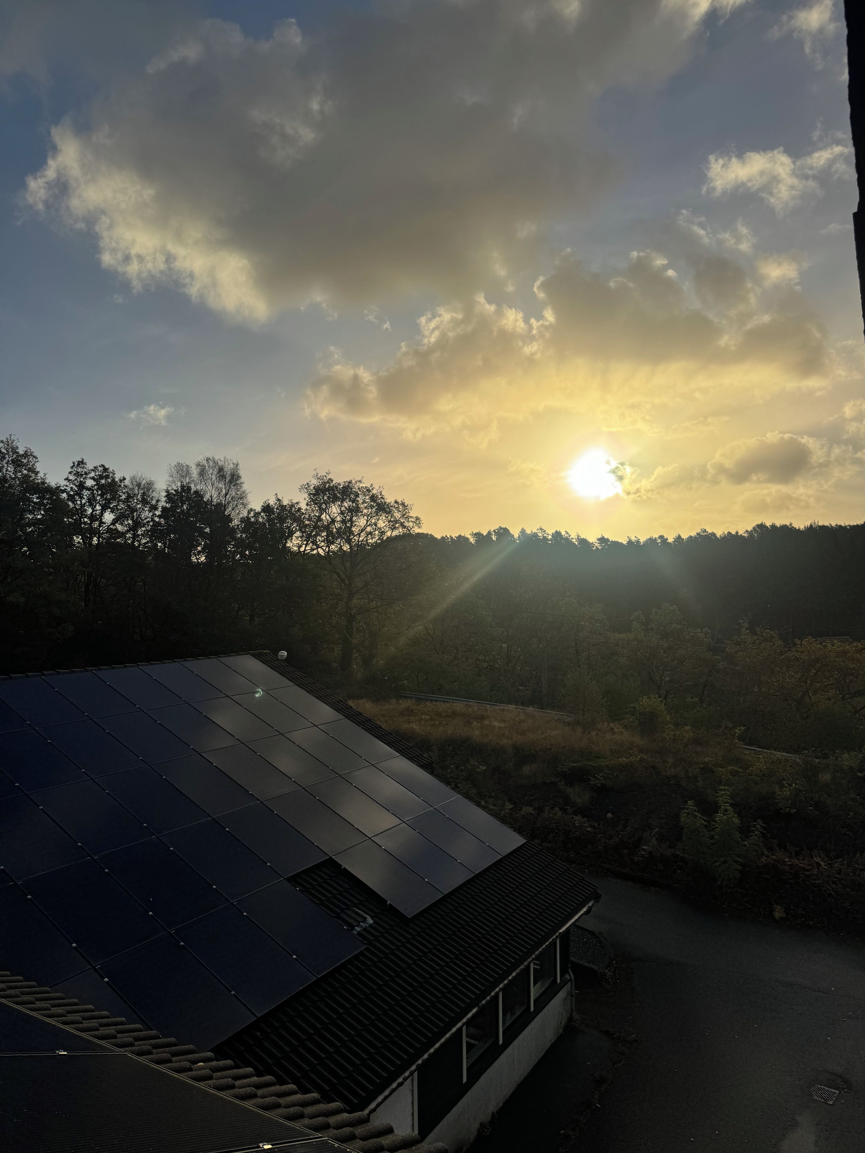 Un bâtiment doté d’un toit en pente et offrant une vue sur le coucher de soleil au-dessus d’une zone boisée.