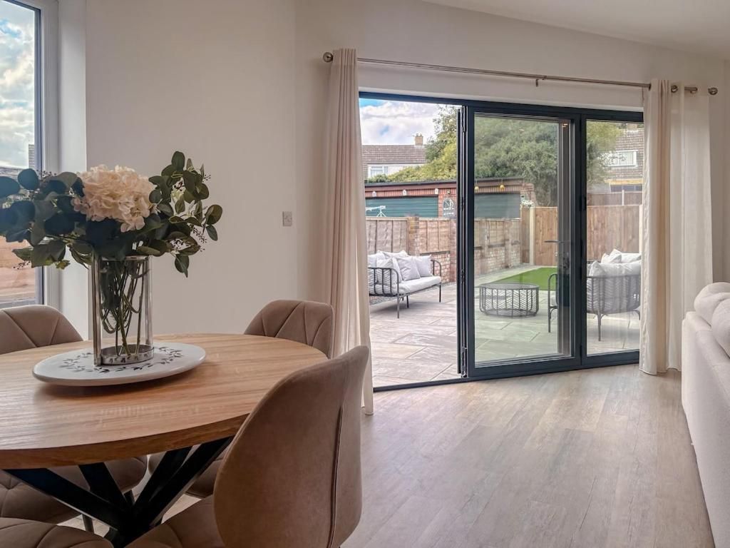 A dining area with a round table and chairs, a vase of flowers, and a sliding glass door leading to an outdoor patio with furniture.