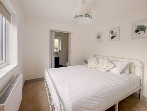 Un dormitorio con cama blanca, un radiador, una puerta y una pared con obras de arte enmarcadas.