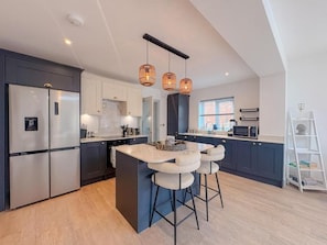 Una cocina moderna con una isla central, taburetes de bar e iluminación colgante.