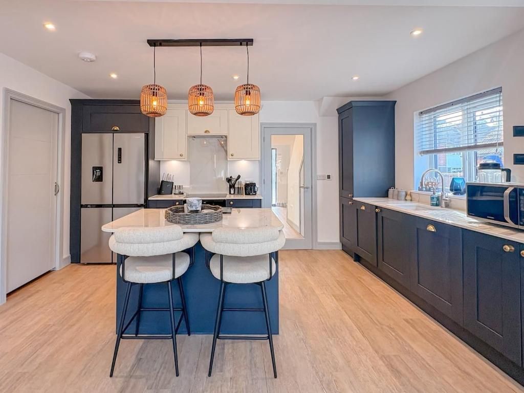 A modern kitchen with a central island, bar stools, pendant lighting, and dark cabinetry.