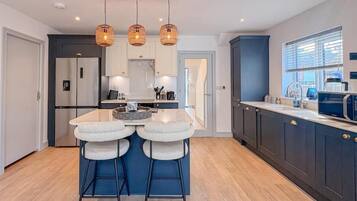 A modern kitchen with a central island, bar stools, pendant lighting, and dark cabinetry.