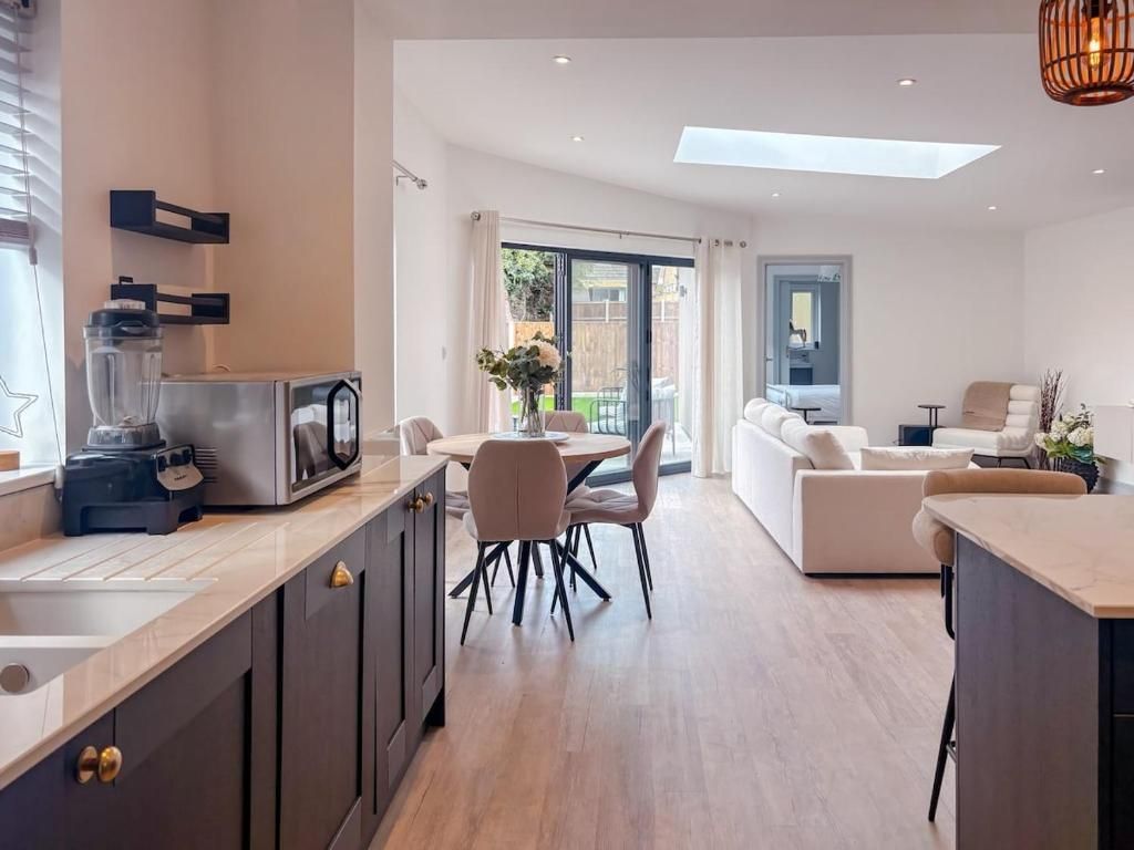 A modern kitchen with a dining area, a sofa, and a view to the outside.