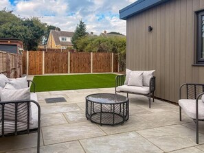 Un espacio de patio con mobiliario exterior, una mesa redonda y vistas a un césped verde y una valla de madera.