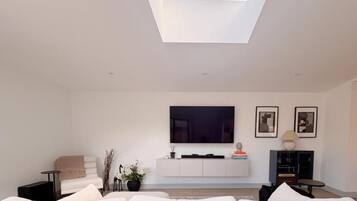 A modern living room with a skylight, a white sofa, a flat-screen TV, and a minimalist decor.