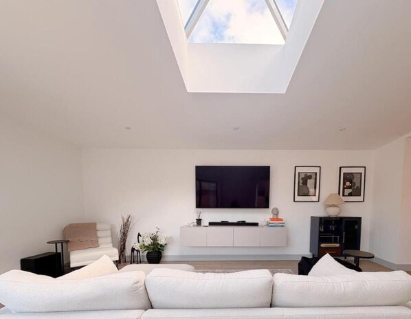 A modern living room with a skylight, a white sofa, a flat-screen TV, and a minimalist decor.