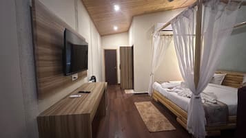 Un dormitorio moderno con televisor de pantalla plana, piso de madera, cama con dosel y ventilador de techo.