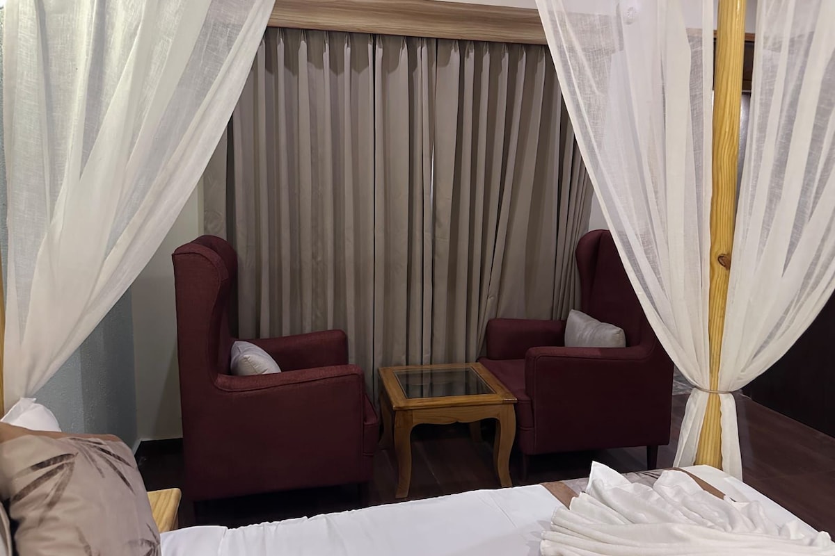 A room with two armchairs, a small table, and a bed with white bedding.