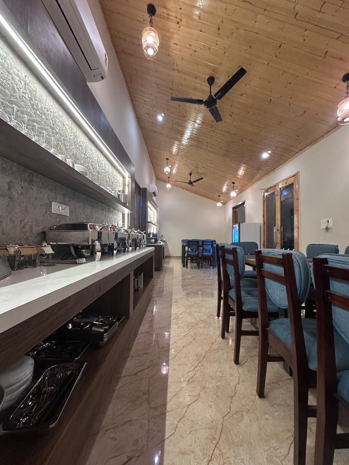 Un restaurante con una barra larga, ventiladores de techo y un comedor con sillas.