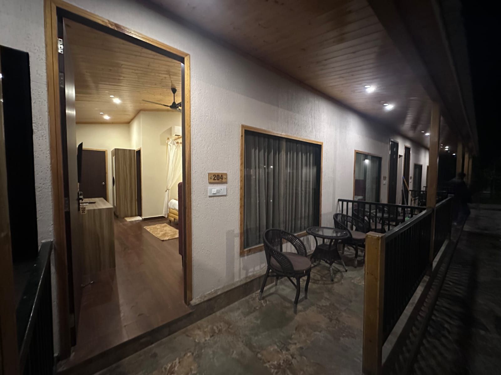 Un pasillo con una puerta de madera que da a una habitación, una pequeña mesa con sillas y una ventana con cortinas.
