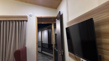 Hotellihuone, jossa on suuri, seinälle asennettu litteänäyttöinen televisio, puinen katto, punainen nojatuoli ja ovi, joka johtaa parvekkeelle.