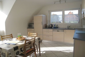 A kitchen with a dining table, chairs, a refrigerator, a microwave, a sink, and a window with a view of a house. - Holiday apartment with 2 bedrooms (Freiburg)