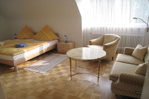 Un dormitorio con cama, mesita de noche, lámpara y una mesa redonda con sillas.