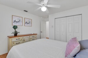 Ein Schlafzimmer mit einem Bett, einem Deckenventilator, einem Schminktisch, zwei gerahmten Motivationssprüchen und einem Kleiderschrank.