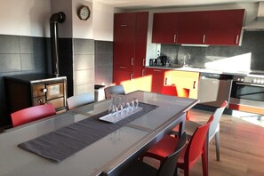 Eine moderne Küche mit roten Schränken, einem Einbauofen und einem Essbereich mit einem Glastisch und Stühlen.