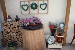 A rustic outdoor setting with a wooden stump adorned with pink flowers, a stack of firewood, and decorative wreaths on the wall. - "Spatz" at the Dold guesthouse (St. Peter)