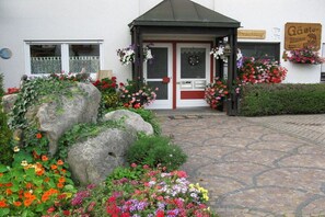 A building with a stone-paved entrance, a red door, and flower boxes on either side. - "Spatz" at the Dold guesthouse (St. Peter)