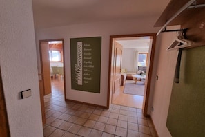 A hallway with a sign listing amenities, leading to a room with a bed and a window. - OG House Thum am Kaiserstuhl (Bötzingen)