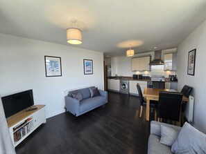 A modern living room with a flat-screen TV, a sofa, a dining table with chairs, and a kitchen area with appliances. - 2BDR Flat Opposite Elstree Studios with Parking (Borehamwood)