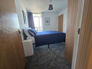 Ein Schlafzimmer mit einem Bett, einem Fenster mit Vorhängen, einer Deckenleuchte und einer Tür.