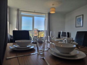 A dining table set with white bowls, plates, and cutlery, with a view of the outdoors through a window. - 2BDR Flat Opposite Elstree Studios with Parking (Borehamwood)