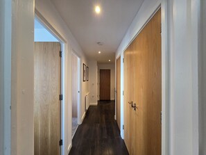 A hallway with wooden doors and a dark floor, leading to a room with a door at the end. - 2BDR Flat Opposite Elstree Studios with Parking (Borehamwood)
