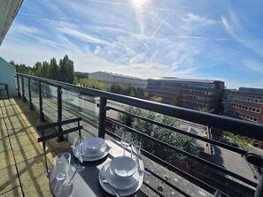 Ein Balkon mit einem Tisch für zwei Personen, der auf einen Parkplatz und Gebäude blickt.