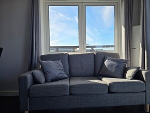 Ein graues Sofa mit Kissen vor einem Fenster mit Blick auf eine Brücke und den Himmel.