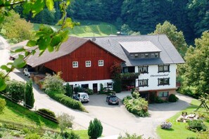Edificio a due piani con una struttura rossa simile a un fienile e un edificio bianco con la scritta 'Christianehof'. Diverse auto sono parcheggiate davanti e la proprietà è circondata dal verde.