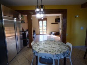 A kitchen with a refrigerator, dining table with chairs, and a view to a living area with a sofa and television. - Holiday Home 'Gîte Lauberoye' with Private Terrace, Private Garden and Wi-Fi (Saint-Pierremont)