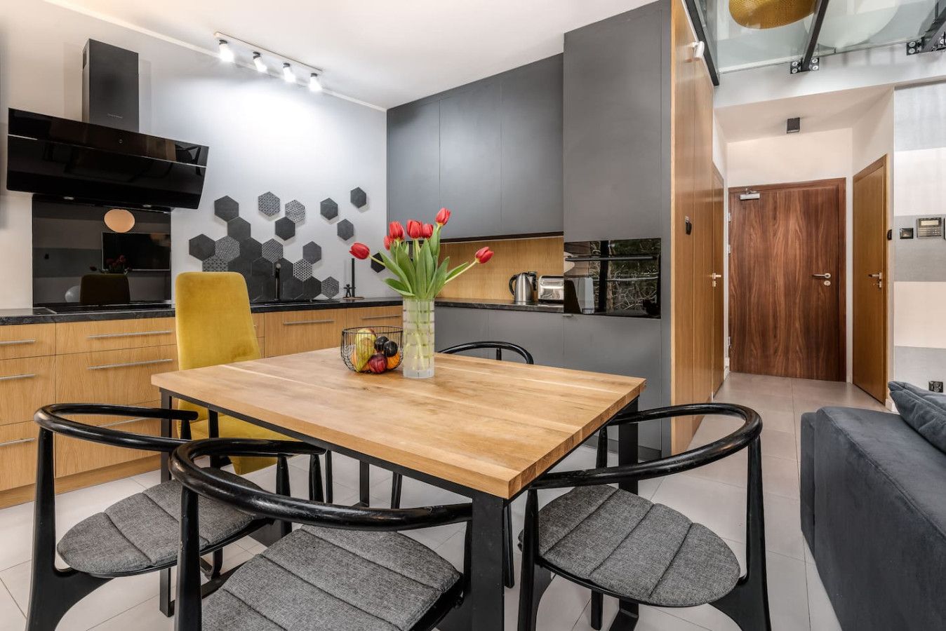 Una cocina moderna con una mesa de comedor de madera, sillas negras y un jarrón con tulipanes rojos.