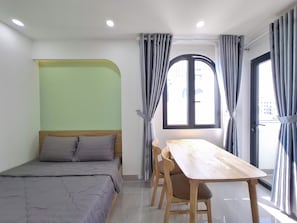 A room with a bed, a dining table with chairs, a window with curtains, and a green accent wall. - Olive House by the Beach - Elevator & Kitchen (Vung tau)
