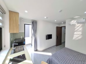 Ein modernes Hotelzimmer mit Bett, Flachbildfernseher, Badezimmer mit Dusche und Küchenzeile.