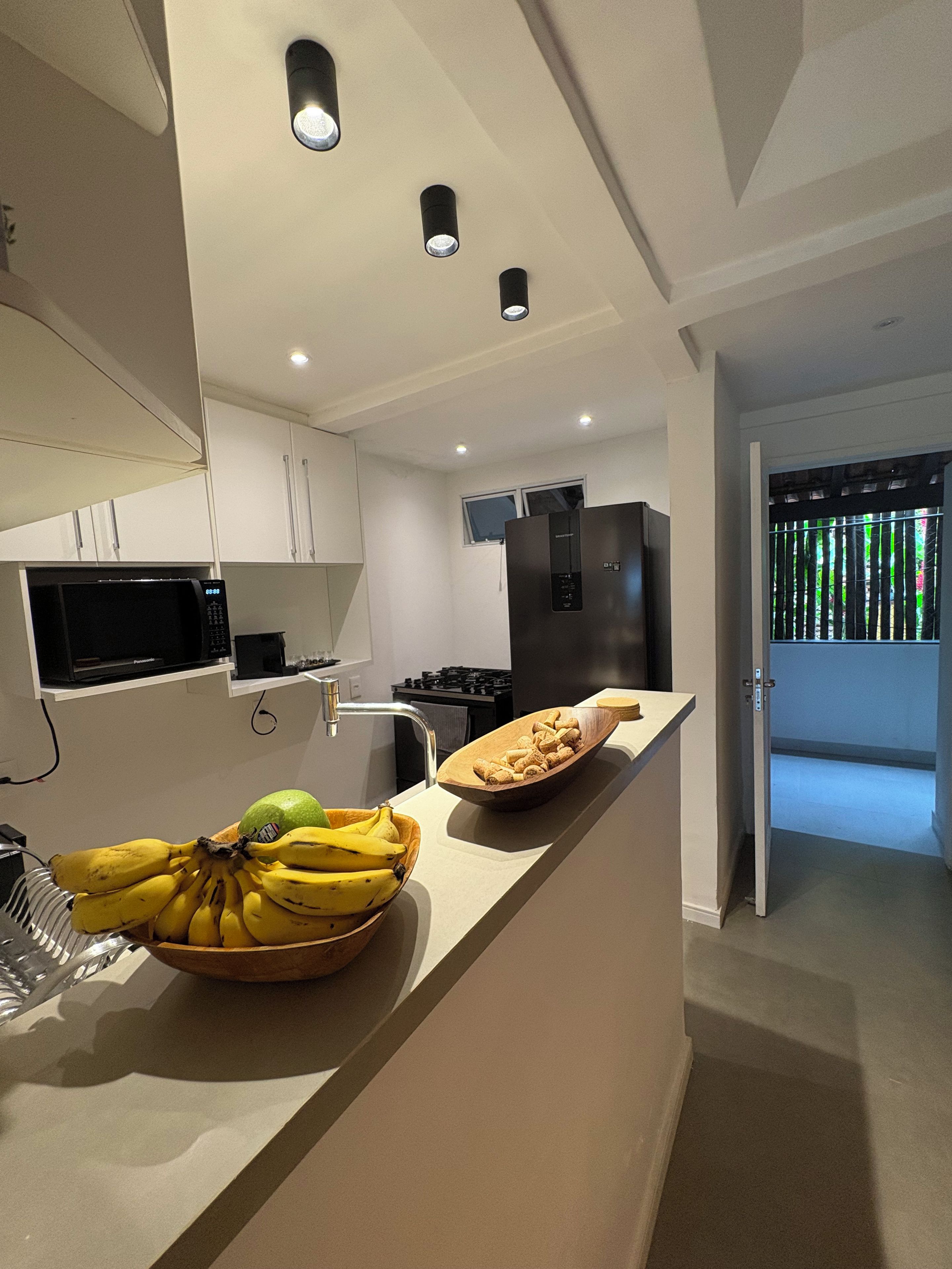 Cozinha moderna com ilha central, eletrodomésticos embutidos e vista para uma varanda.