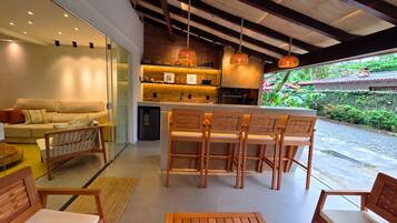 Een moderne keuken met een bar, een eethoek met houten stoelen en uitzicht op een weelderige tuin.