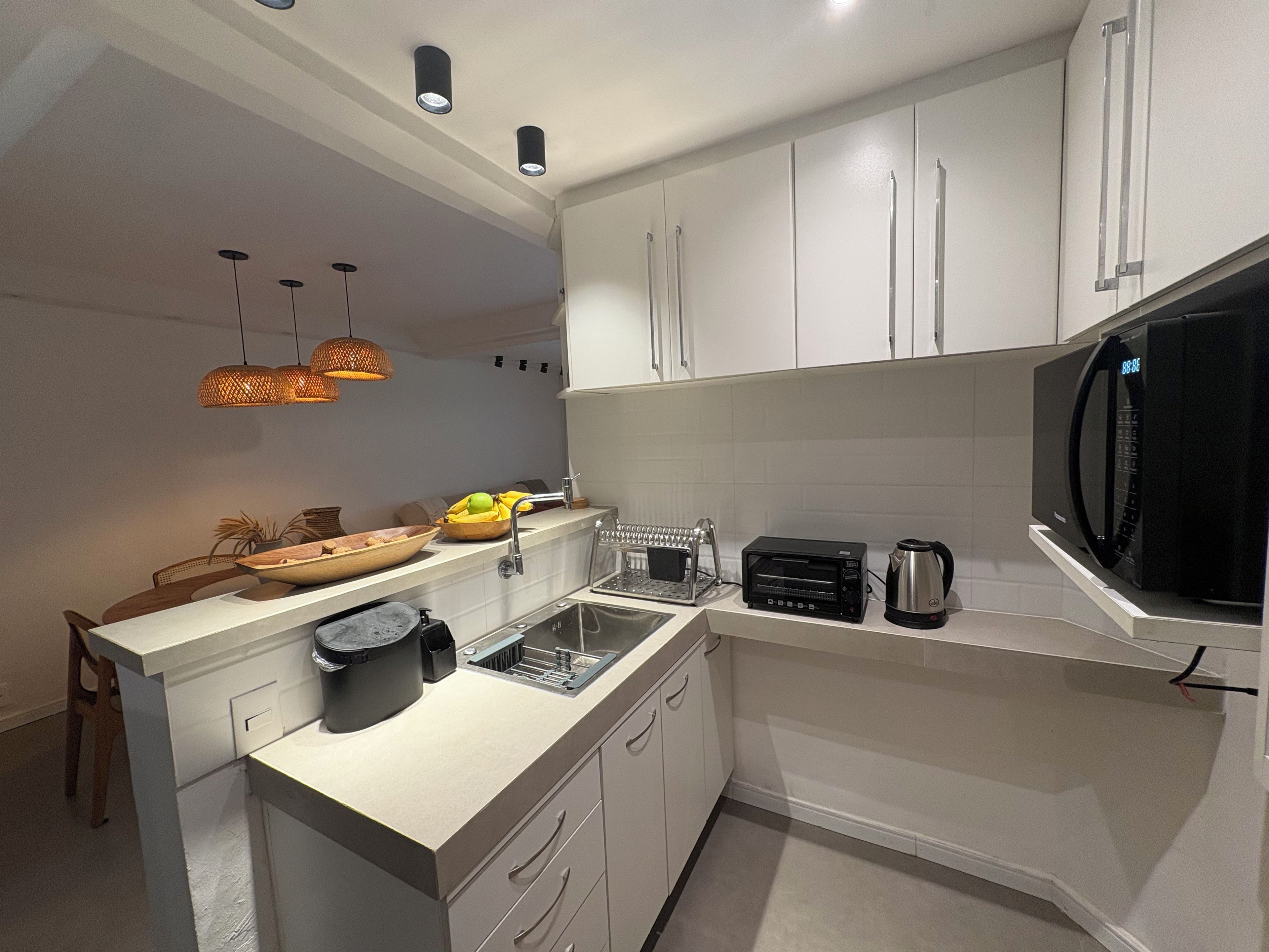 Une cuisine moderne avec des meubles blancs, un micro-ondes noir, un grille-pain et un évier.