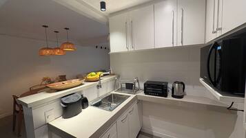 Une cuisine moderne avec des meubles blancs, un micro-ondes noir, un grille-pain et un évier.