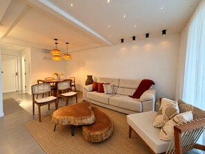 A modern living room with a sofa, coffee table, and dining area. - Porto Frade Stay • Angra • Privet Gourmet Lounge • Golf, Marina & Beach Access (Angra dos Reis)