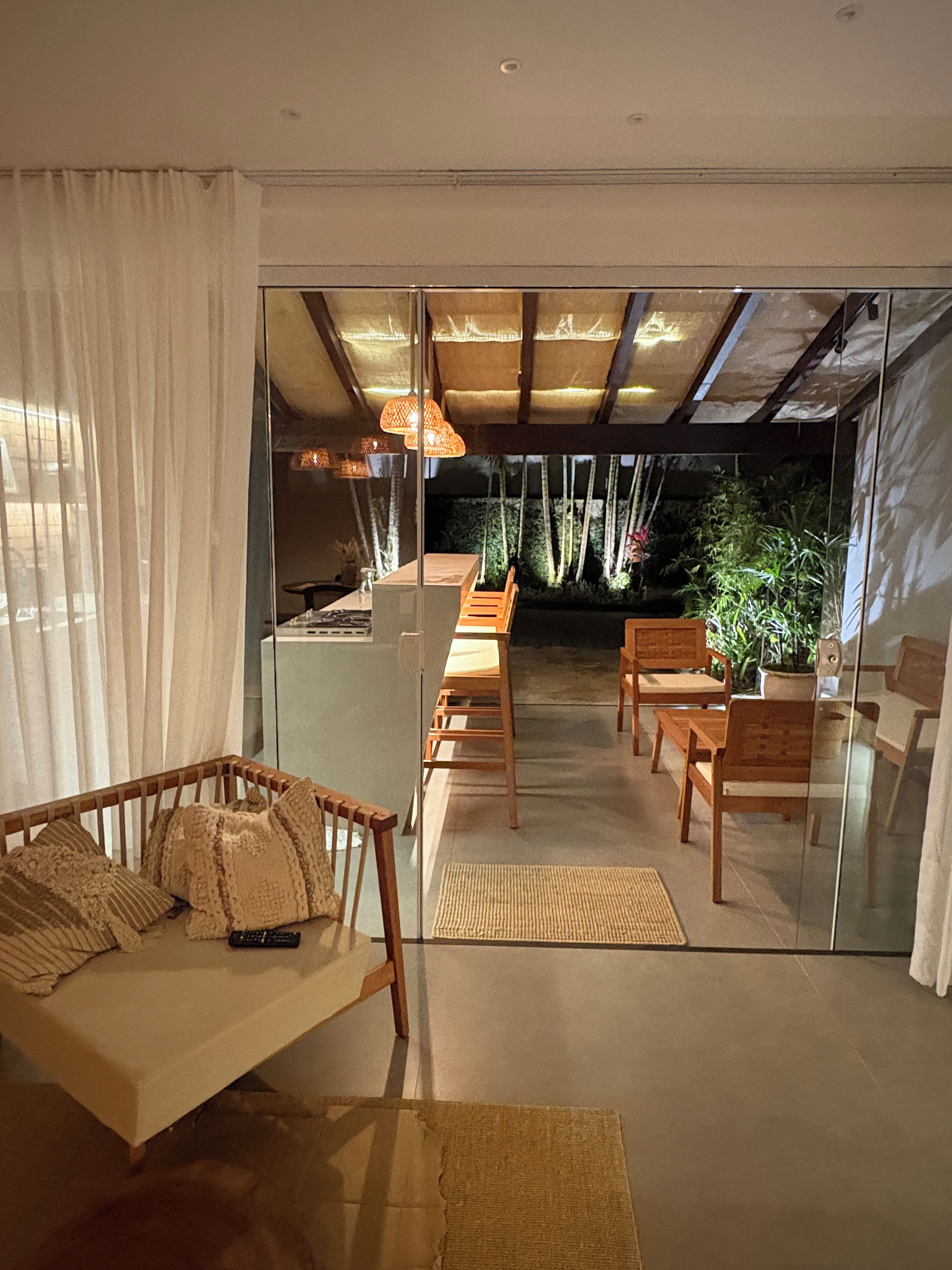 Interior moderno com divisória de vidro, mobiliário de madeira e vista para um jardim.