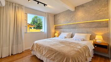 Une chambre à coucher avec un grand lit, deux tables de chevet avec des lampes, une fenêtre avec des rideaux et une vue sur l’extérieur.