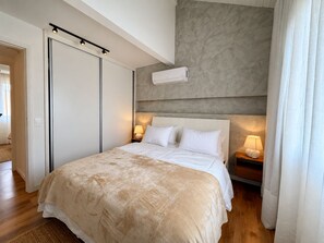 A modern bedroom with a large bed, a ceiling-mounted air conditioner, and bedside lamps.