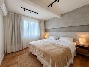 A modern bedroom with a large bed, bedside lamps, a ceiling light, and a window with sheer curtains.