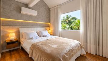 Une chambre d’hôtel avec un lit, des lampes de chevet, un appareil de climatisation, une fenêtre avec des rideaux et une vue sur la verdure environnante.