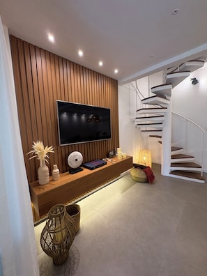Una sala de estar moderna con un televisor de pantalla plana montado en una pared de madera, una escalera espiral blanca y una cesta tejida en el suelo.